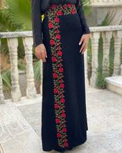 Black dress with red floral embroidery on a stone pavement.